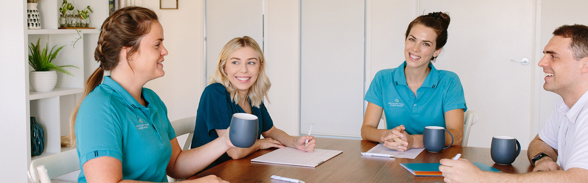 Careers - Group of four happy SSRG clinicians holding a meeting around a table with cups of tea and paperwork