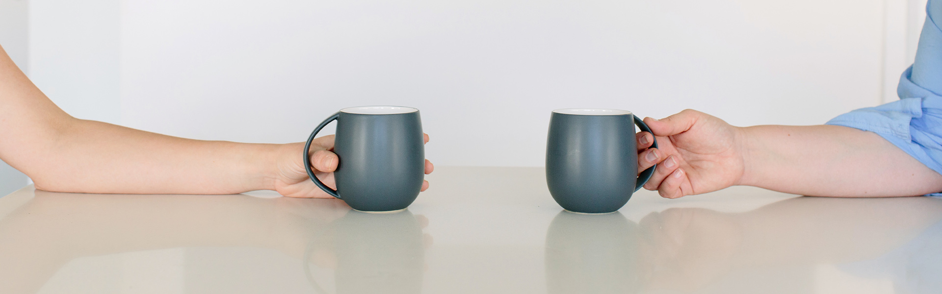 Close up of two hands holding coffee cups during a social work appointment