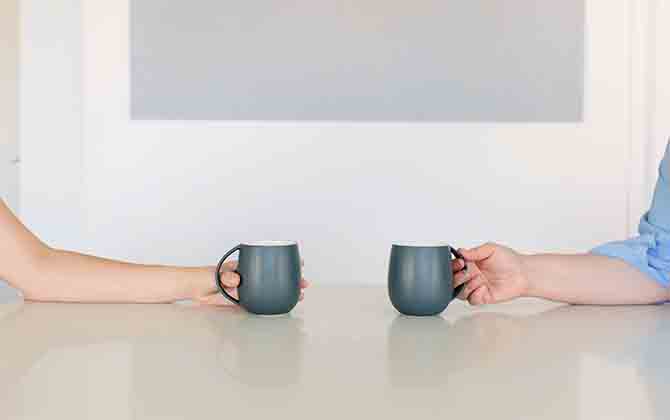 Two hands holding cups as two people sit opposite each other