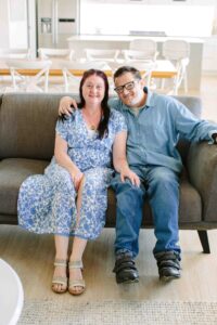 Disability and inclusion image featuring a two people with disability on couch smiling at camera